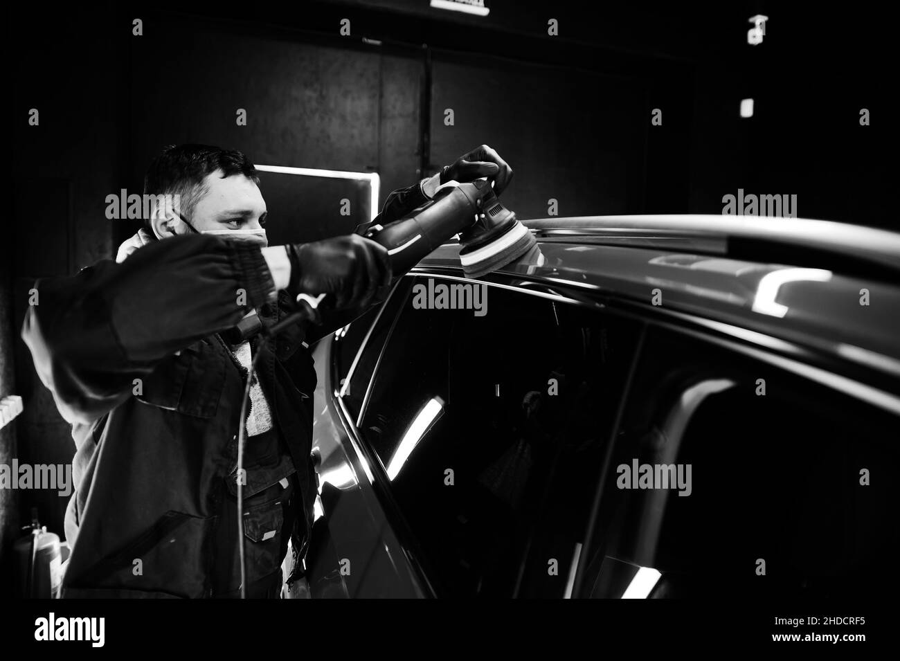 Concepto de detalle de coches. Hombre en máscara de cara con pulidor orbital en taller de reparación puliendo coche naranja suv. Foto de stock