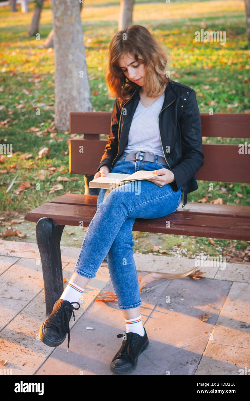 Alegre niña adolescente leyendo libro en banco en el parque de otoño Foto de stock