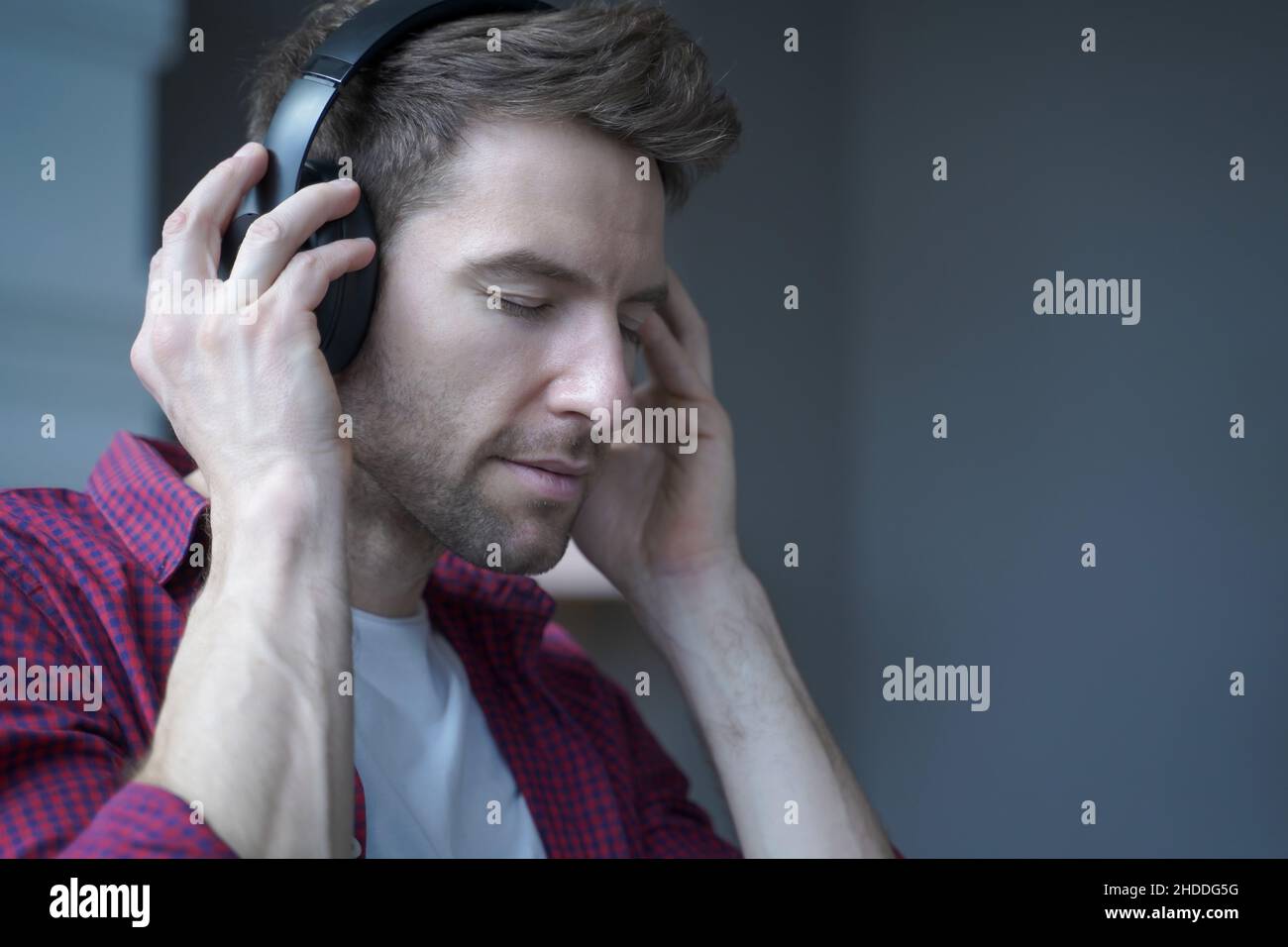 Joven alemán contento con los ojos cerrados escuchando música en los auriculares en casa con cara encantada Foto de stock