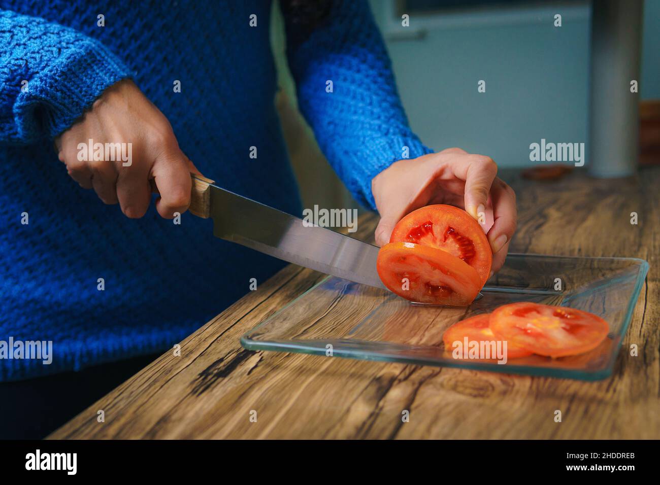 En la mesa hay una tabla de cortar y se puede ver las manos de una mujer cortando cebollas blancas con un cuchillo de chef. Foto de stock
