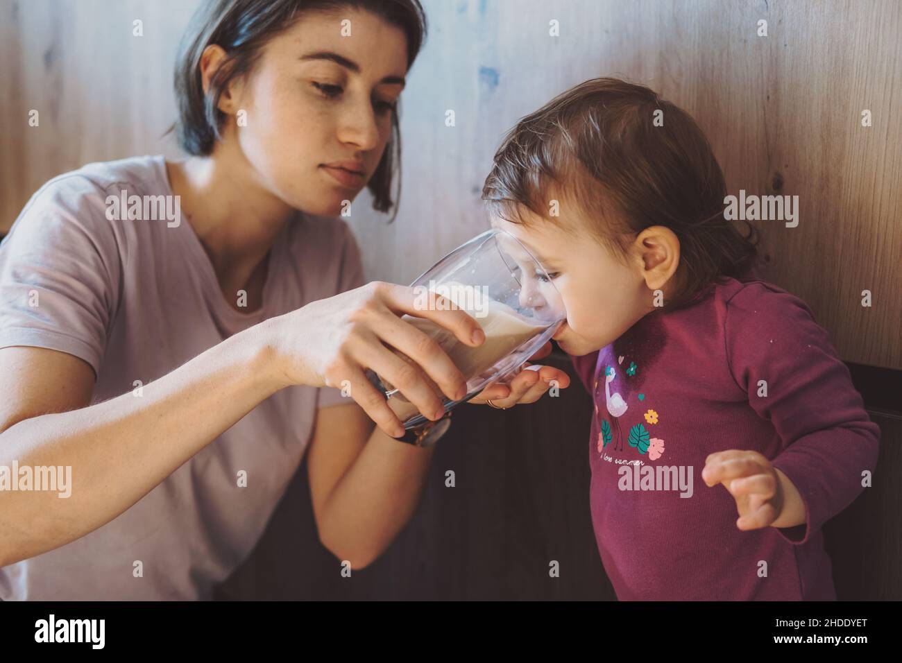 Madre dándole a la chica un vaso de leche para beber. Atención materna. Infancia. Foto de stock