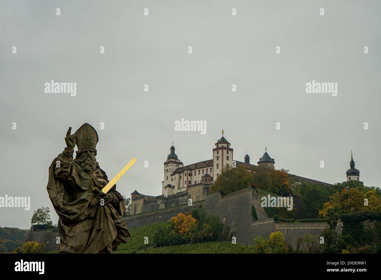 Una escultura que lleva una espada brillante dorada en su mano izquierda.El brazo derecho se levanta con un dedo índice de advertencia. Würzburg Marienberg fortaleza detrás. Foto de stock
