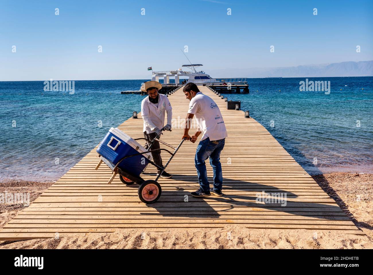 Dos hombres en un embarcadero que llevan suministros a un barco turístico en el Berenice Beach Club, Aqaba, provincia de Aqaba, Jordania. Foto de stock