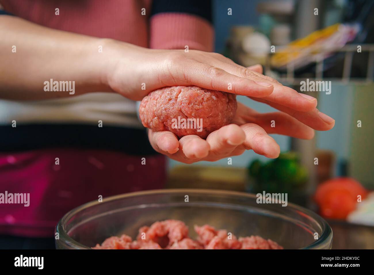 Primer plano de las manos de una mujer preparando carne molida para hacer hamburguesas, la carne sigue cruda y está añadiendo los ingredientes, agradable atmósfera en el Foto de stock