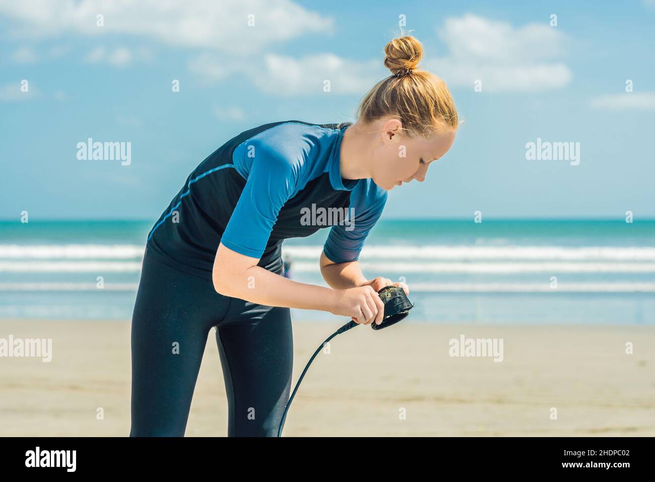 Tiempo de verano y concepto de descanso activo. Joven mujer surfista principiante fastens correa a través de la pierna, yendo a surfear en grandes olas barral en el océano, dreseed adentro Foto de stock
