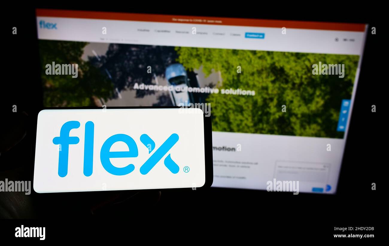 Persona que sostiene el smartphone con el logotipo de la compañía electrónica Flex Ltd. En la pantalla frente al sitio web. Enfoque en la pantalla del teléfono. Foto de stock