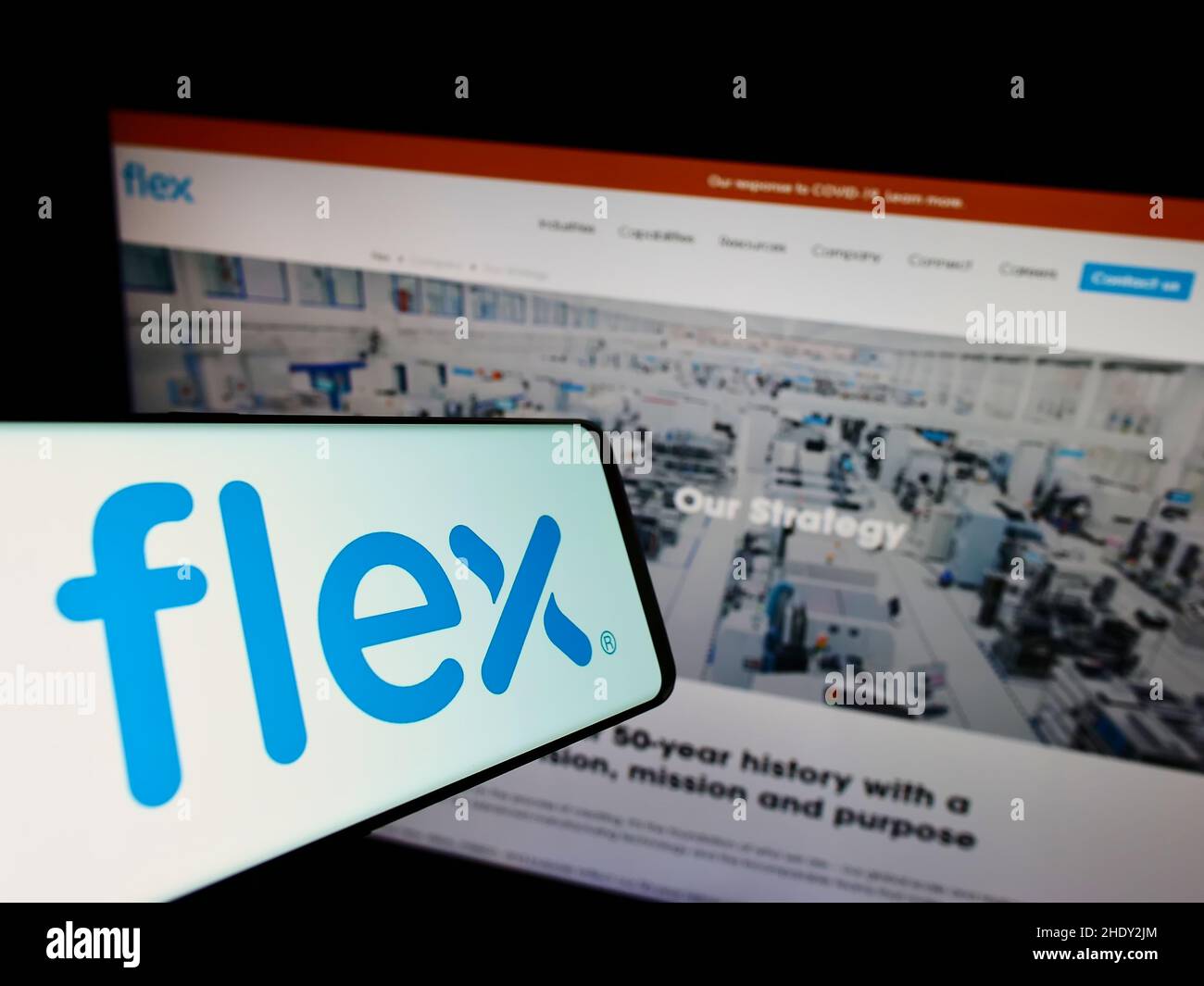 Teléfono móvil con el logotipo de la empresa electrónica Flex Ltd. En la pantalla frente al sitio web de negocios. Enfoque en la parte central derecha de la pantalla del teléfono. Foto de stock