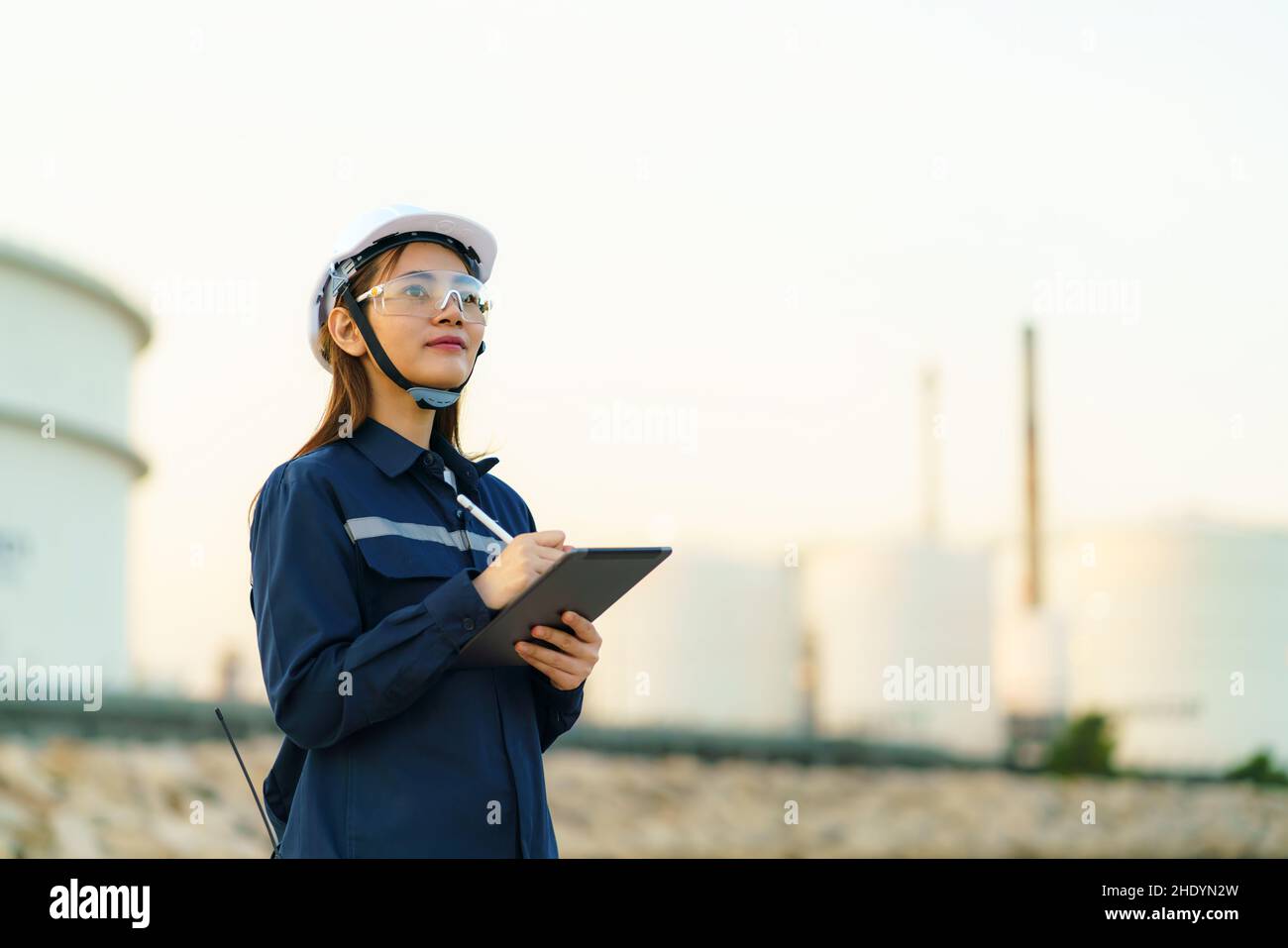 Una ingeniera asiática está comprobando el mantenimiento de la fábrica de refinería de petróleo por la noche a través de tabletas digitales. Foto de stock