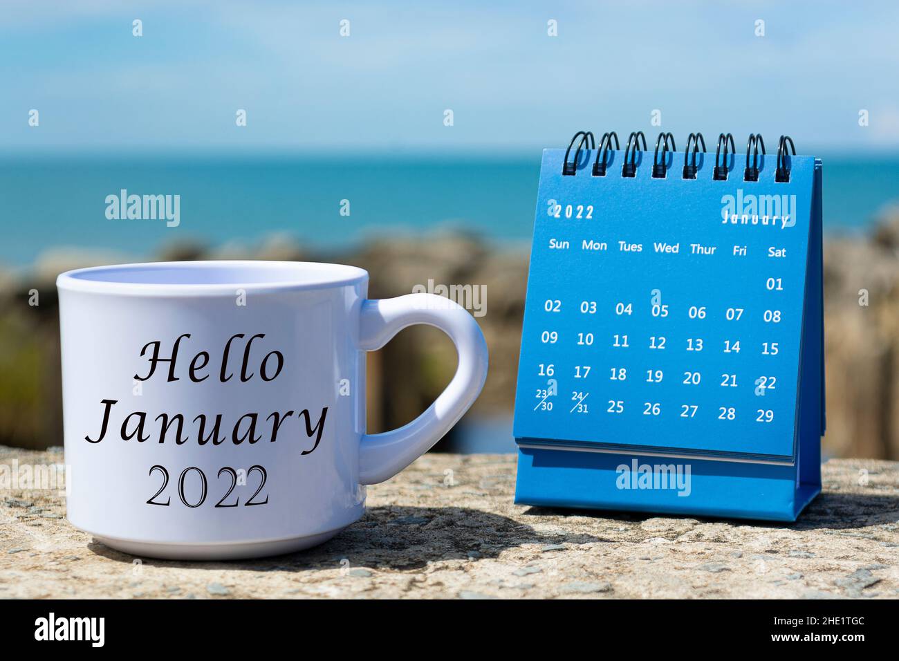 Hola Enero 2022 Escrito en taza de café blanco con calendario azul y fondo  del océano. Concepto de año nuevo Fotografía de stock - Alamy