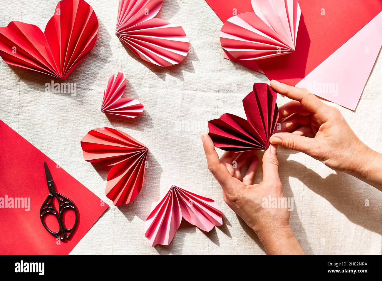 Las manos de la mujer hacen corazones de papel. Guirnalda de origami.  Símbolo de amor por el día de San Valentín, feliz cumpleaños, saludos, Día  de la Madre, Día de la Mujer.
