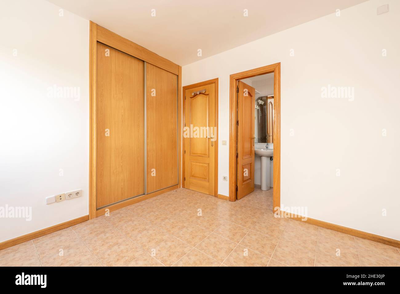 habitación con carpintería de roble, armario empotrado con puertas correderas y baño Foto de stock