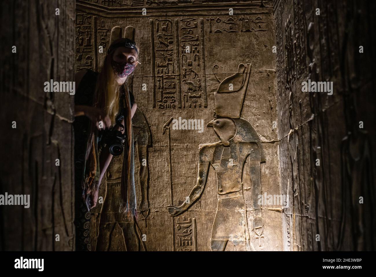 Una turista femenina mira a la vuelta de la esquina en un pasaje débilmente iluminado dentro de un antiguo templo egipcio en Egipto. Foto de stock