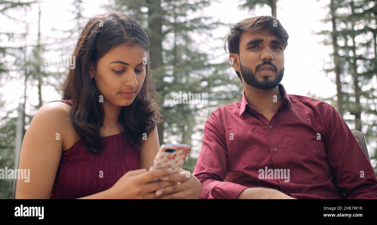 Una joven india comprobando su teléfono mientras estaba en una cita con su novio en un parque Foto de stock