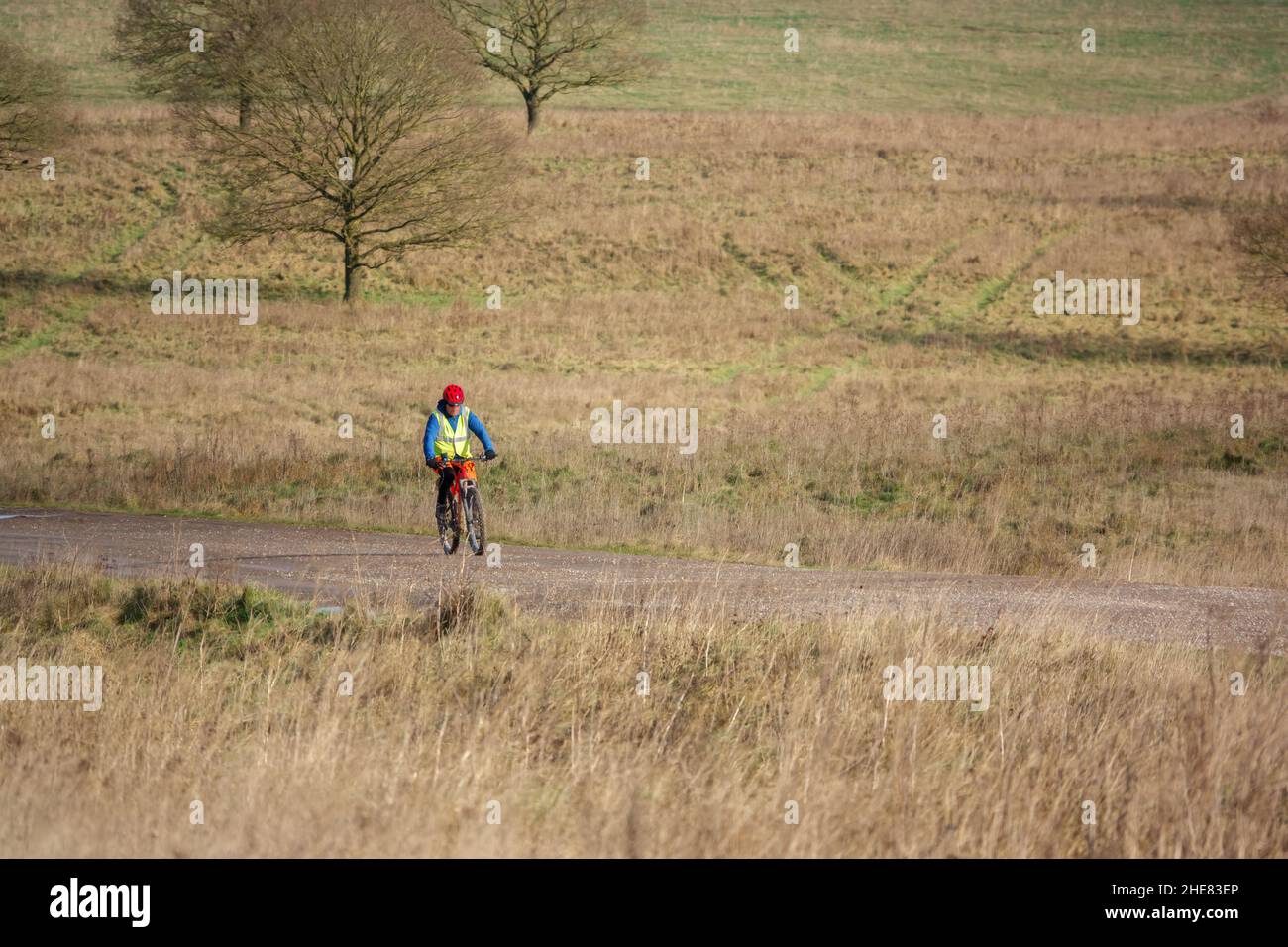 Un ciclista informal que lleva una chaqueta amarilla de alta visibilidad en una pista de piedra que cruza la llanura de salisbury, Wiltshire UK Foto de stock