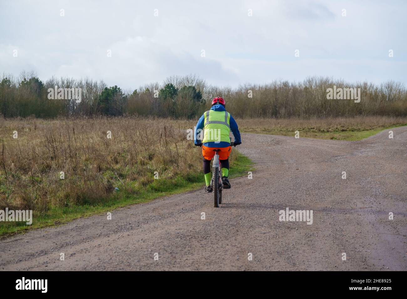 Un ciclista informal que lleva una chaqueta amarilla de alta visibilidad en una pista de piedra que cruza la llanura de salisbury, Wiltshire UK Foto de stock