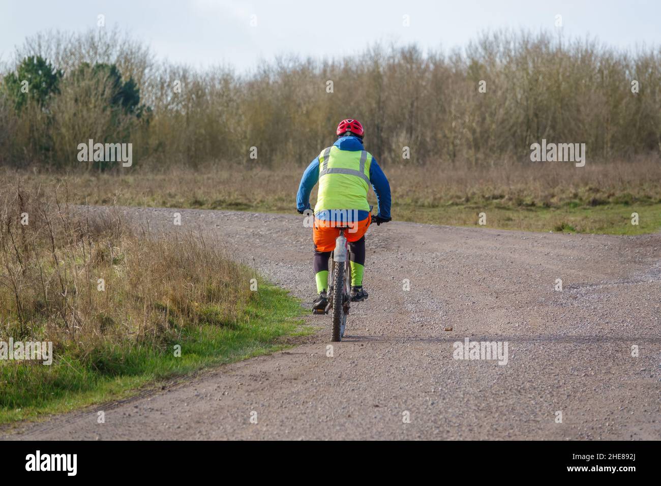 Un ciclista informal que lleva una chaqueta amarilla de alta visibilidad en una pista de piedra que cruza la llanura de salisbury, Wiltshire UK Foto de stock