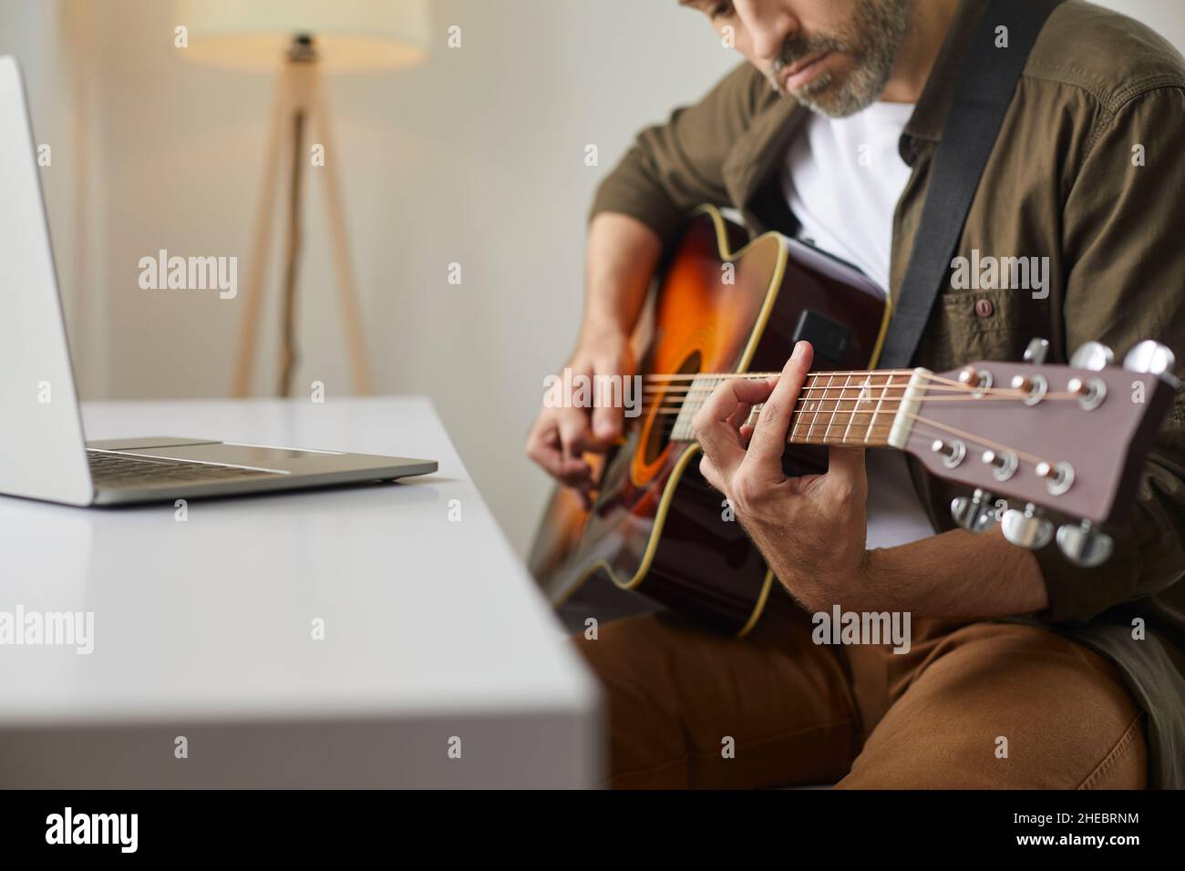 Hombre aprendiendo a tocar la guitarra acústica y viendo video tutorial en  el portátil en casa Fotografía de stock - Alamy
