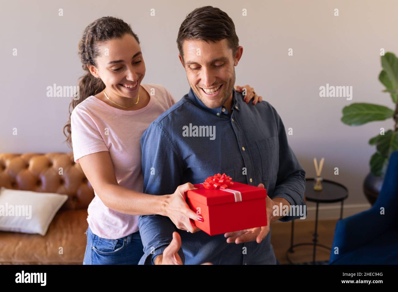 Mujer caucásica sorprendiendo a su marido con un regalo en casa Foto de stock