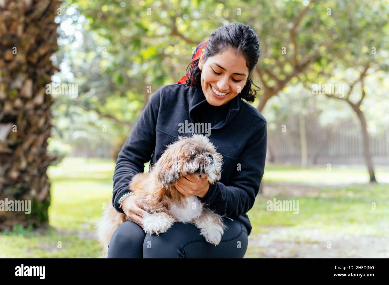 Linda mujer joven está abrazando a su pequeño cachorro. Amor entre el dueño y el perro. Foto al aire libre en el parque, enfoque selectivo. Concepto de estilo de vida Foto de stock