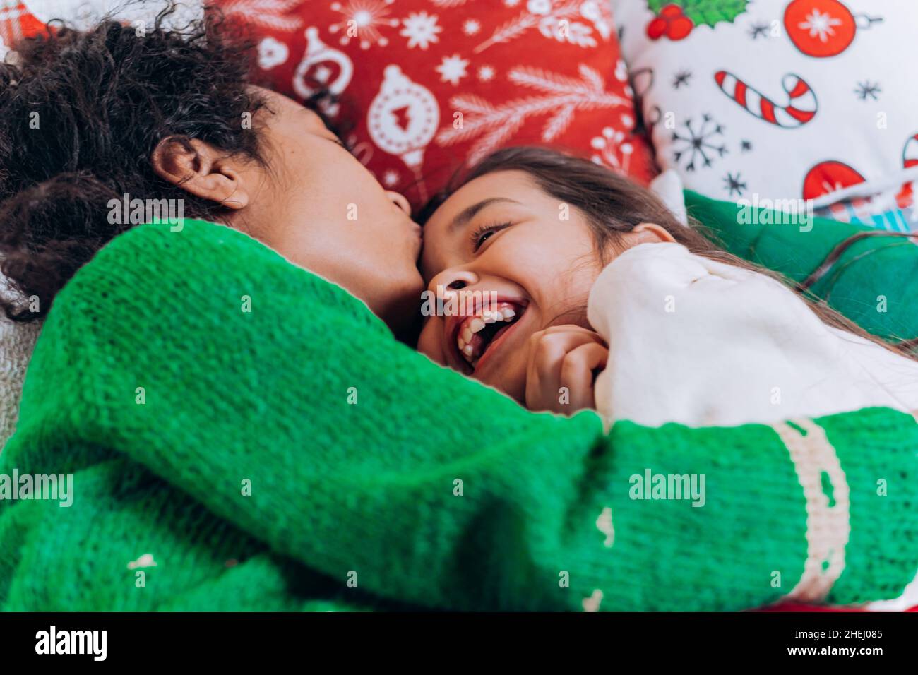 La madre afroamericana con pelo rizado abraza a la hija morena y se ríe acostada en almohadas en la comodidad de la sala de estar en Navidad Foto de stock