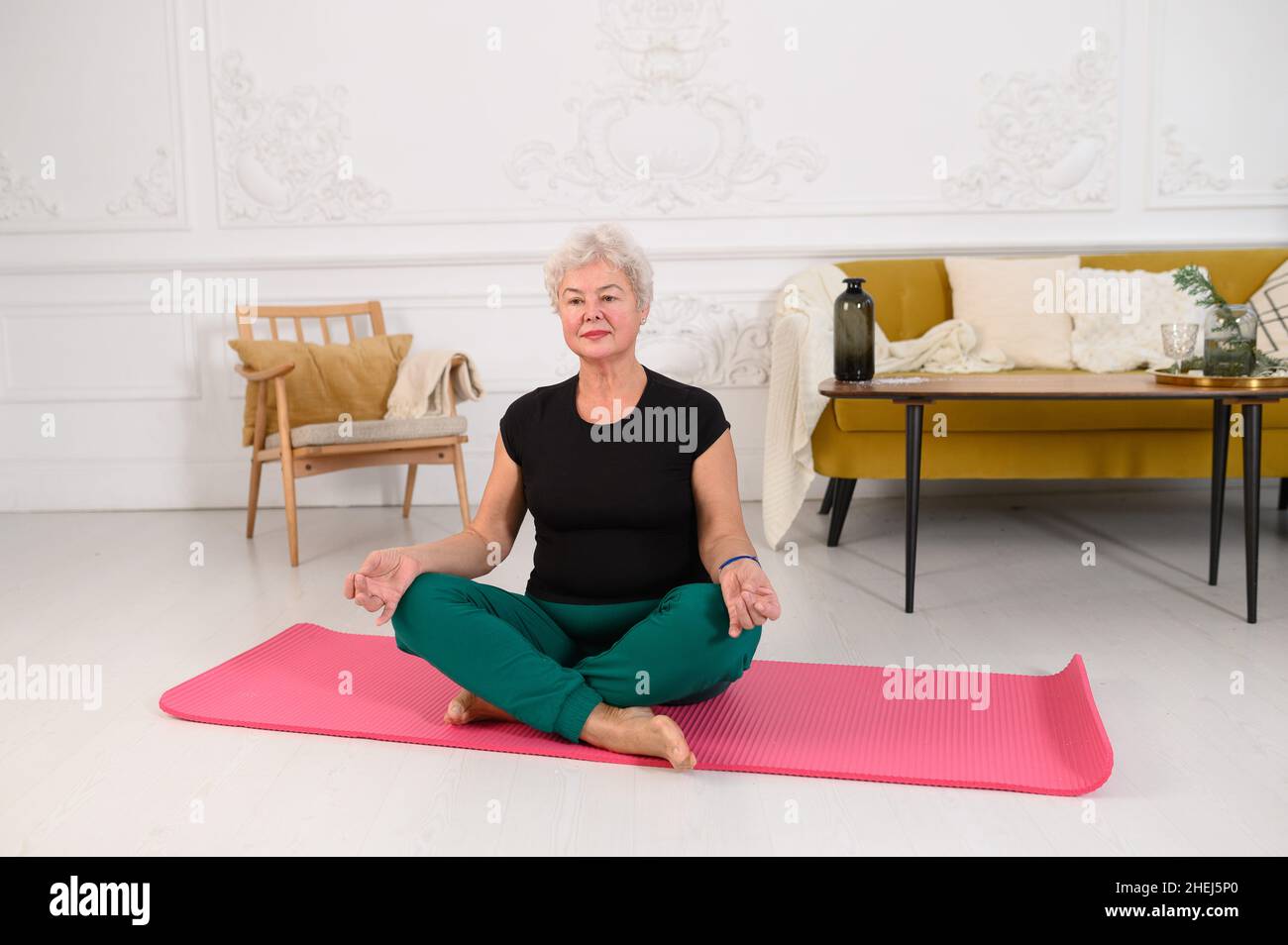 Una mujer mayor deportiva haciendo yoga mientras ve un tutorial en el portátil Foto de stock