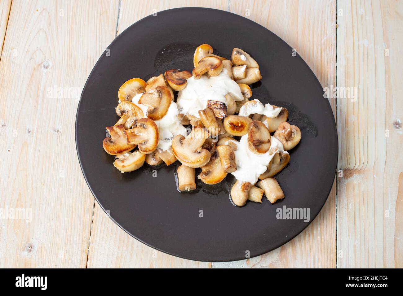 Champiñones champiñones fritos con crema agria y ajo, en un plato negro irregular, vista superior Foto de stock