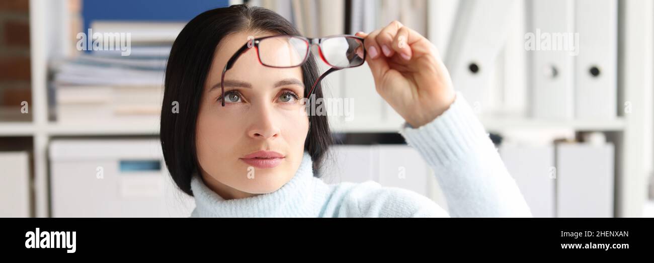 La mujer se quita y mira las gafas mientras está sentada en el lugar de trabajo Foto de stock