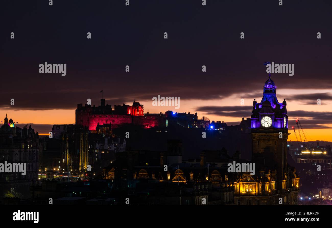 Castillo de Edimburgo y la torre del reloj Balmoral iluminados por la noche con la colorida puesta de sol, Edimburgo, Escocia, Reino Unido Foto de stock