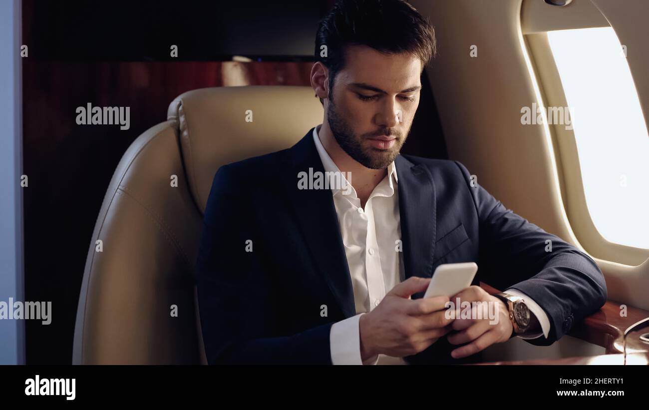 Hombre de negocios con smartphone en avión privado Foto de stock