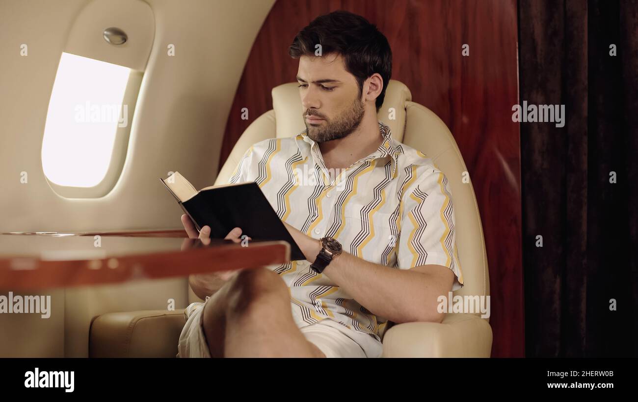Hombre barbudo leyendo libro en avión privado Foto de stock