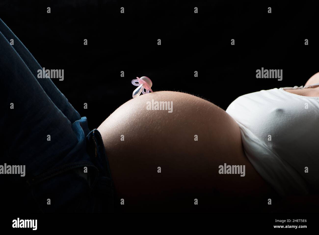 chupete rosa sobre el vientre de la mujer embarazada sobre fondo negro Foto de stock
