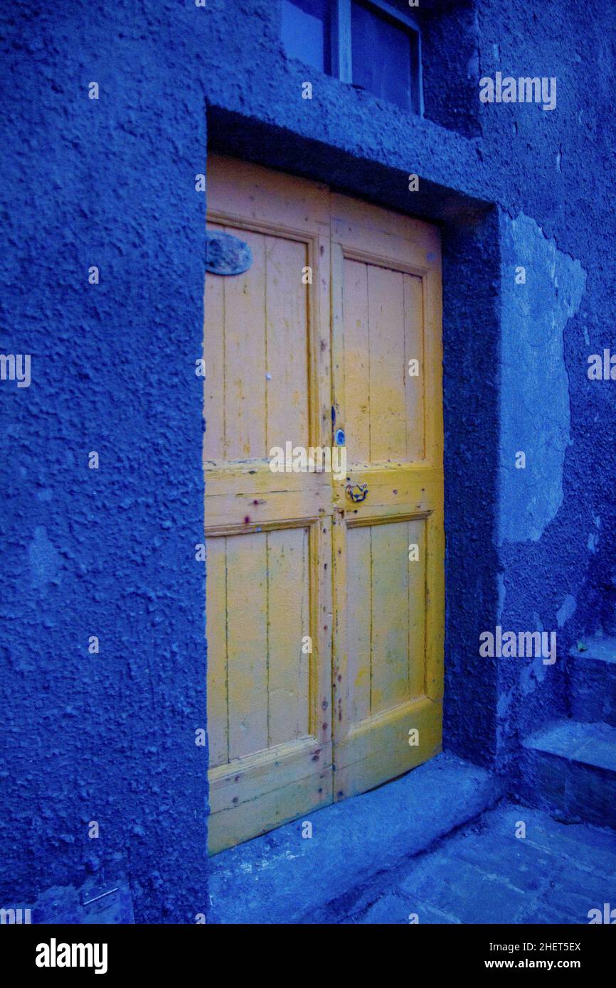 Antiguo edificio de estuco azul italiano con una antigua puerta amarilla Foto de stock