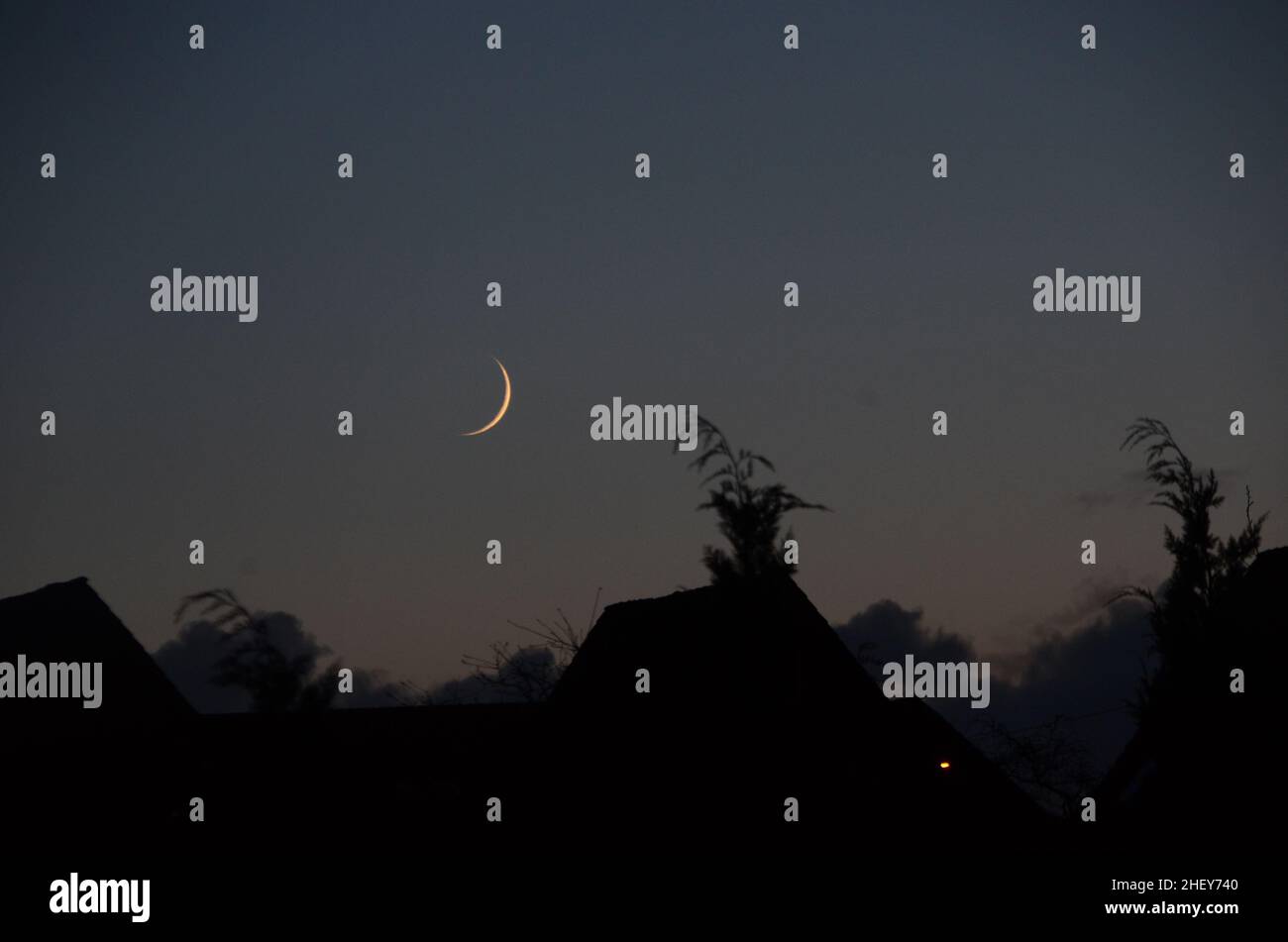 La Luna Nueva vista al atardecer sobre las siluetas de un asentamiento. Foto de stock