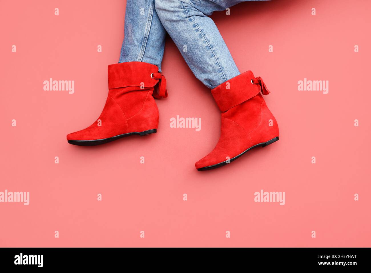 Patas caucásicas para mujer con jeans azules y botas de piel de ante rojo  de ángulo corto sin tacones fondo de color rojo carmesí. Espacio de copia,  vista frontal superior Fotografía de