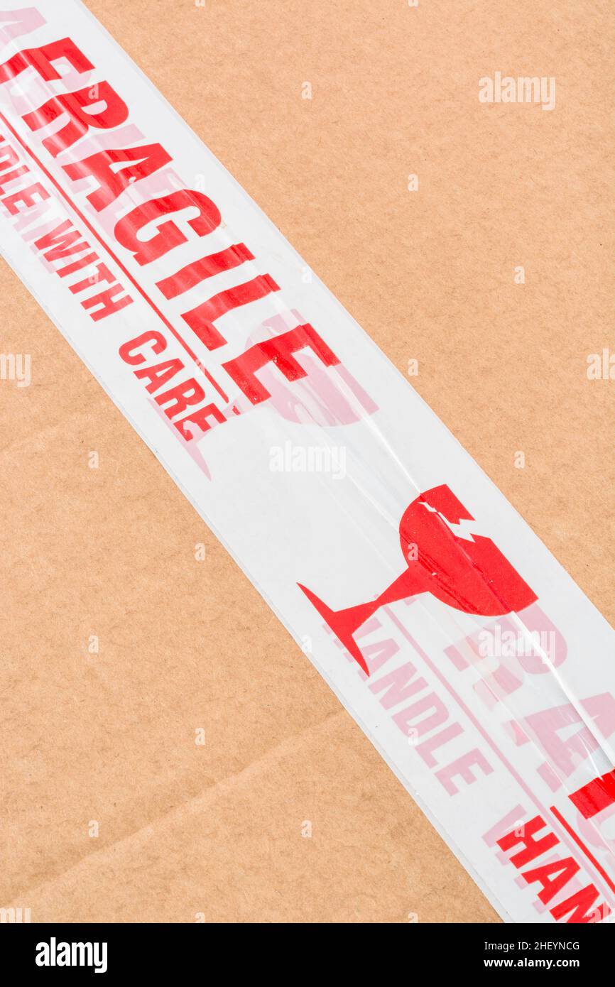 Caja de envío de cartón marrón con cinta adhesiva de plástico de polipropileno rojo y blanco 'Fragile Handle with Care'. Por algo frágil. Foto de stock