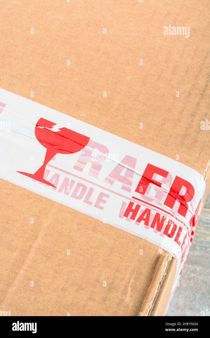 Caja de envío de cartón marrón con cinta adhesiva de plástico de polipropileno rojo y blanco 'Fragile Handle with Care'. Por algo frágil. Foto de stock