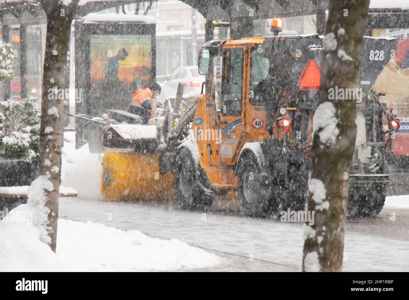 Belgrado, Serbia - 11 de enero de 2022: Quitar y limpiar un polvo nevado ligero de la calle de la ciudad con vehículo de escoba de nieve en la acera, mantenimiento de invierno Foto de stock