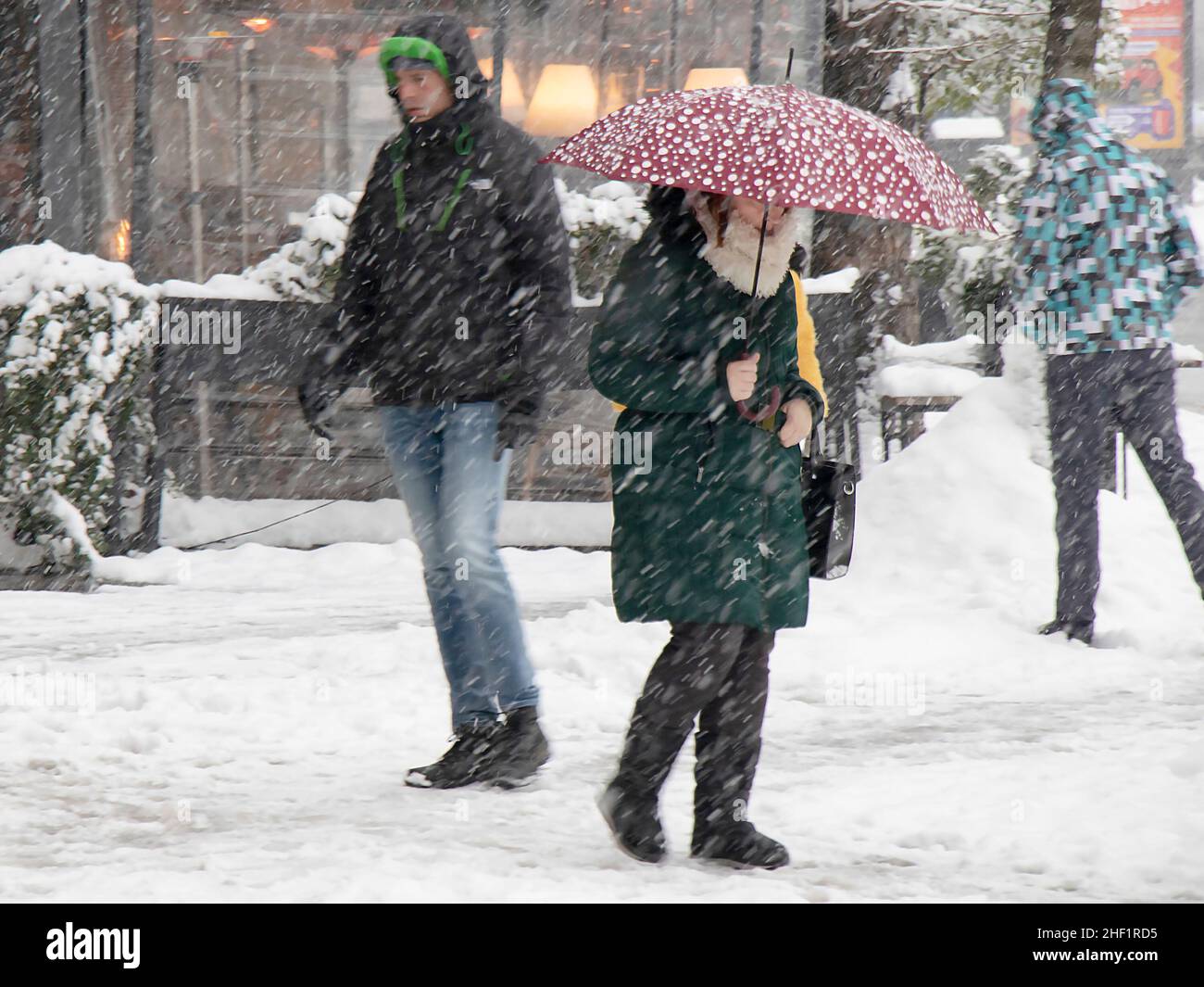 Belgrado, Serbia - 11 de enero de 2022: Personas caminando por la calle nevada de la ciudad durante fuertes nevadas, y una mujer está sosteniendo un paraguas rojo Foto de stock