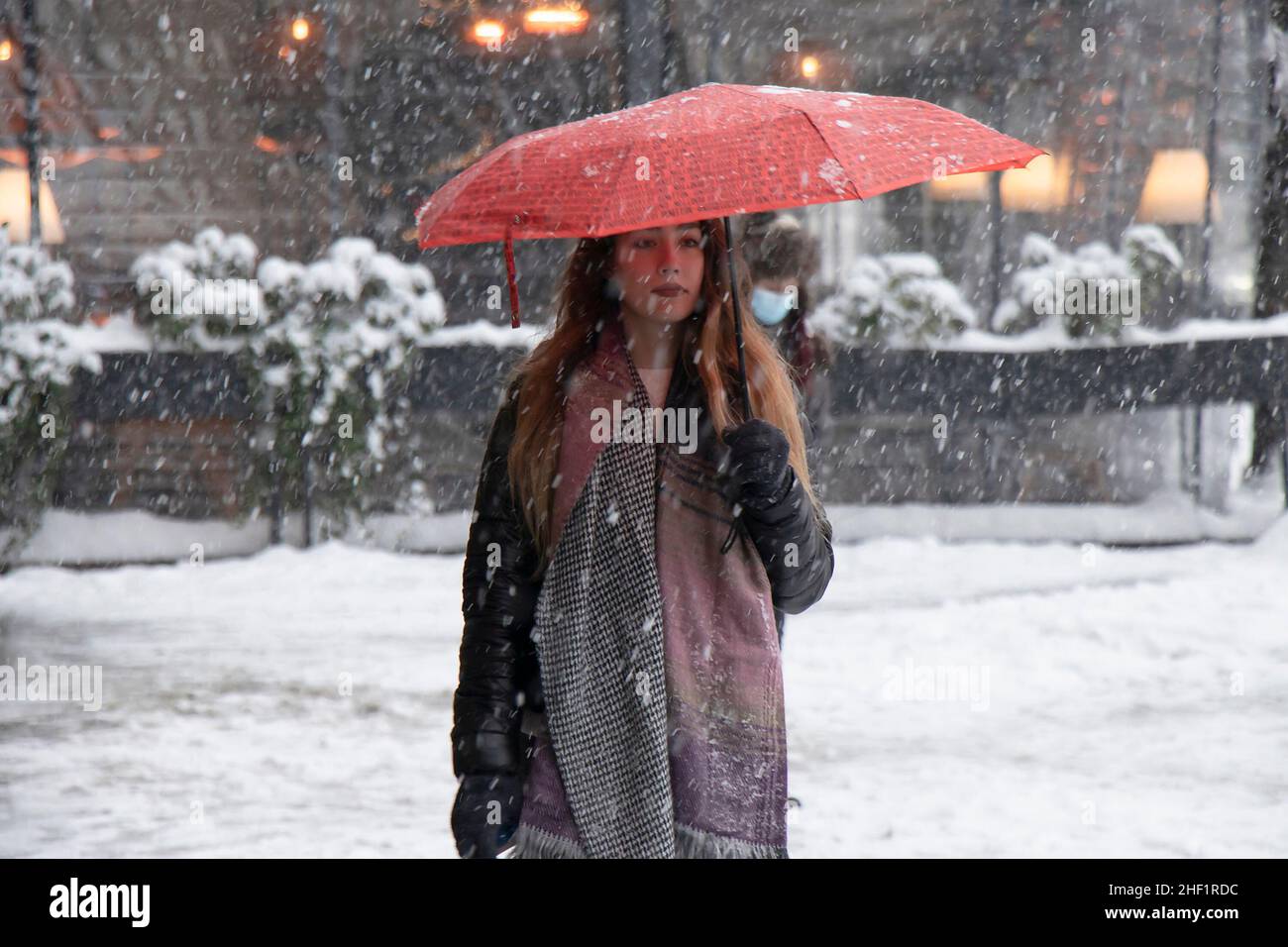 Belgrado, Serbia - 11 de enero de 2022: Una joven caminando bajo un paraguas rojo en un día nevado de invierno en la ciudad Foto de stock