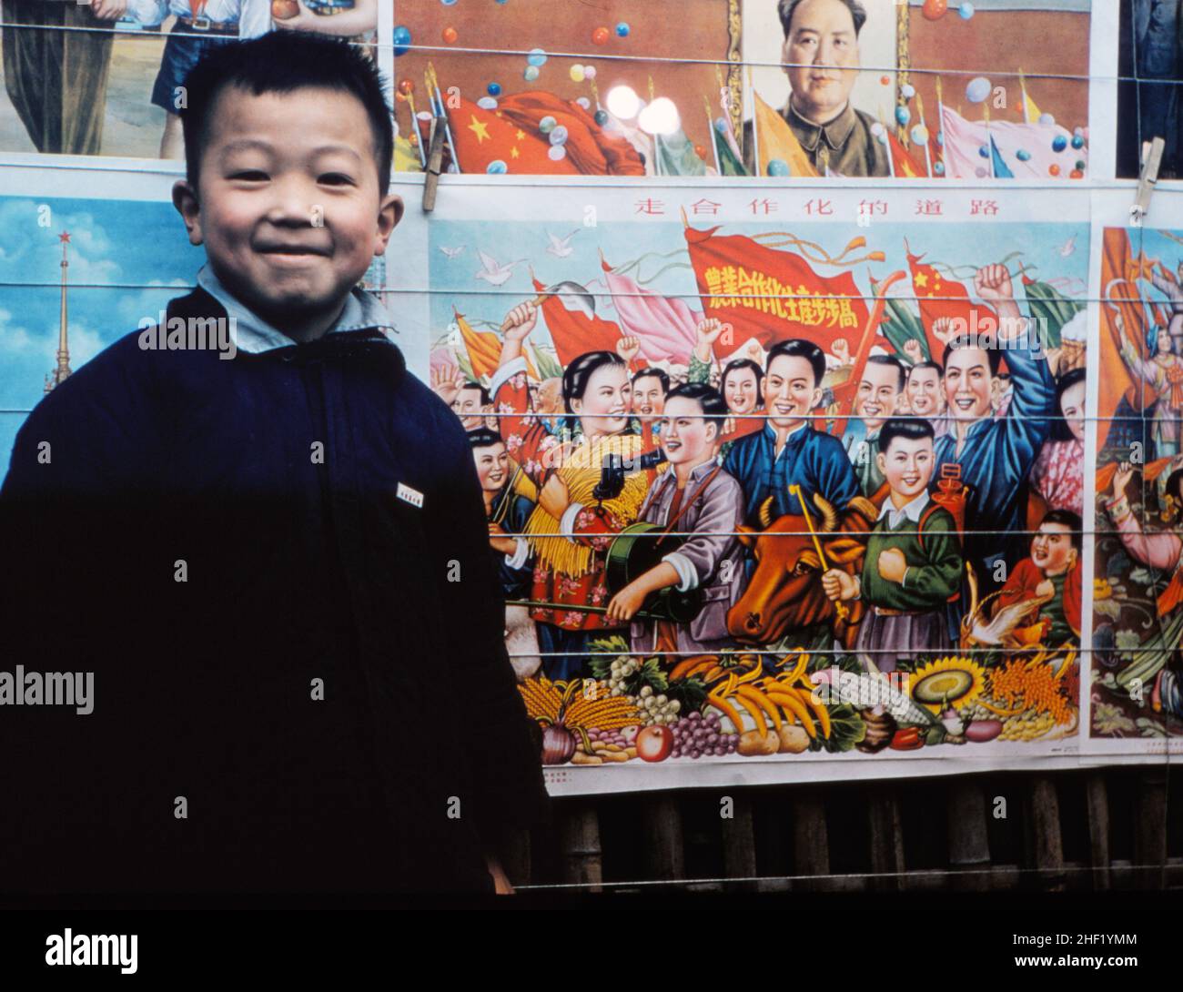 Niño en Beijing, 1957 años, con carteles que muestran a los trabajadores prósperos y felices Foto de stock