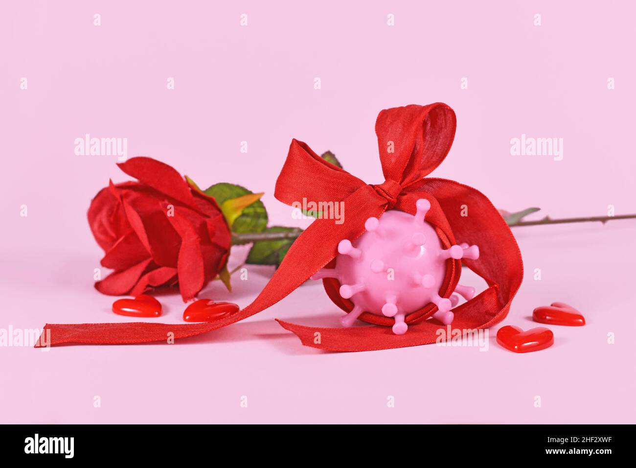 Día de San Valentín durante el concepto de pandemia de Corona con modelo de virus envuelto en cinta y rosa sobre fondo rosa Foto de stock