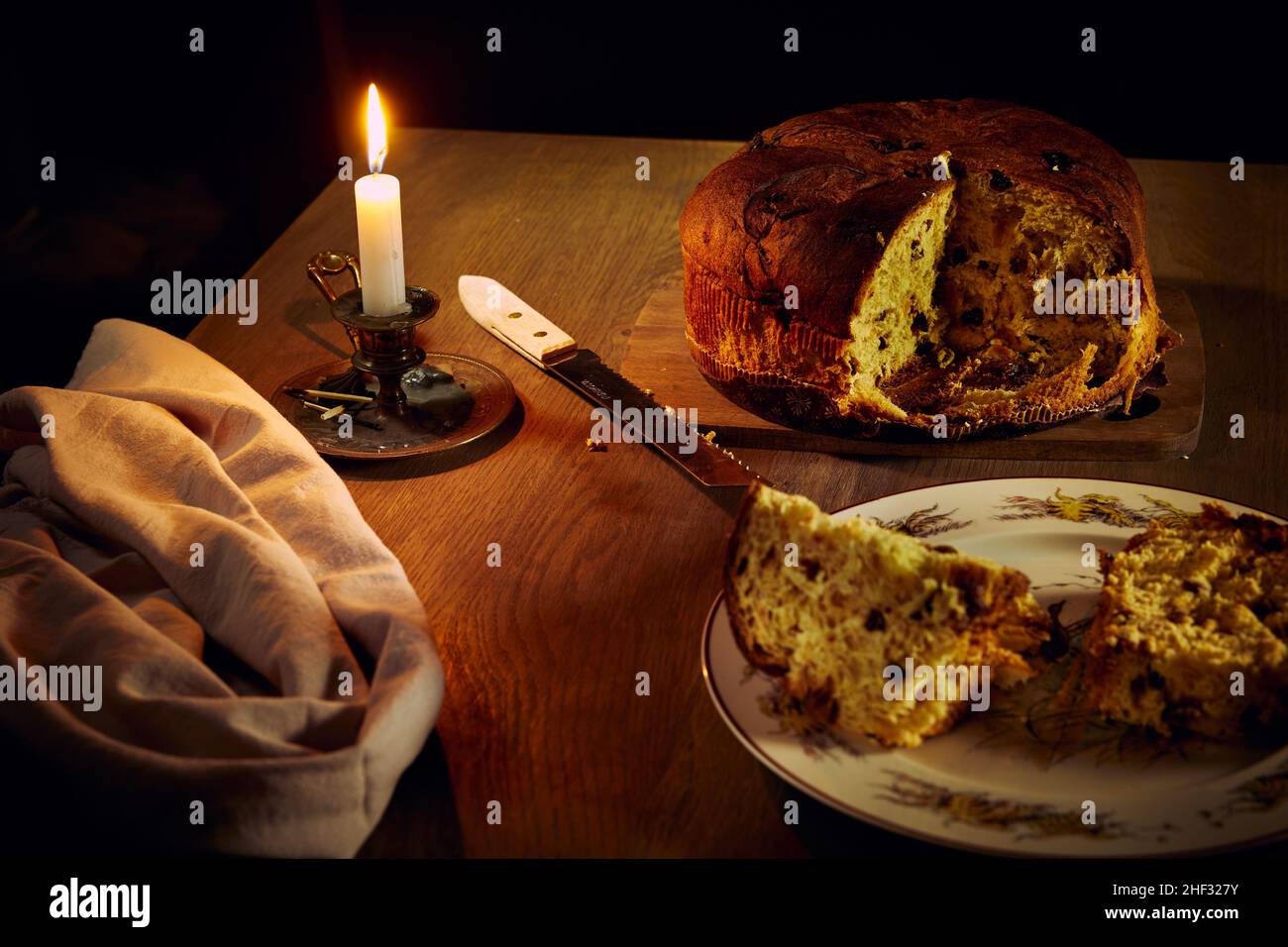 Composición con panettone cortado La especialidad italiana pastel de Navidad con pasas y bayas en una mesa de madera con velas encendidas Foto de stock