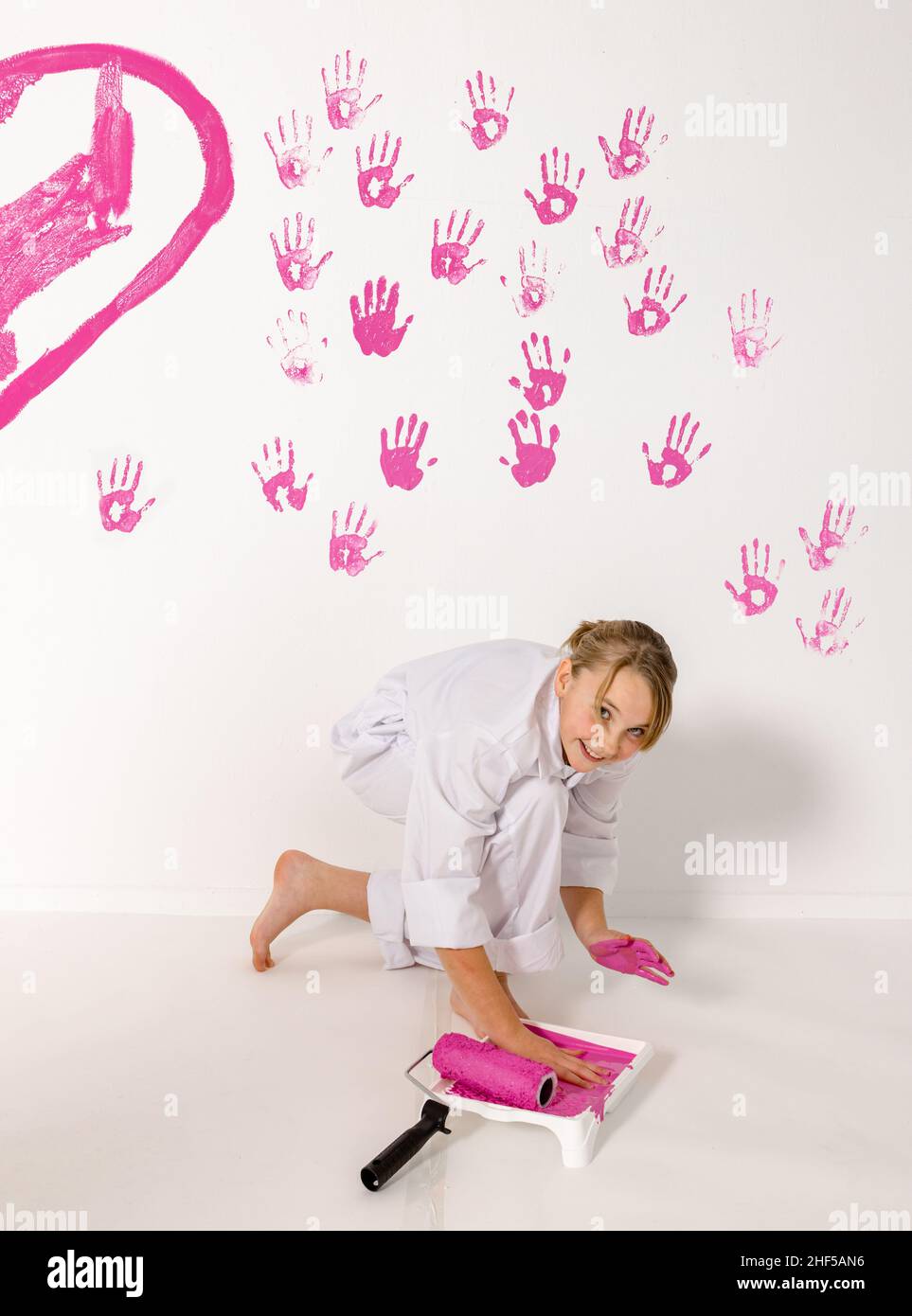 niña de 10 años pintando con sus manos sobre una pared blanca. La pinta es rosa y la pared es blanca. La chica tiene una expresión feliz mirando en la cámara. Foto de stock