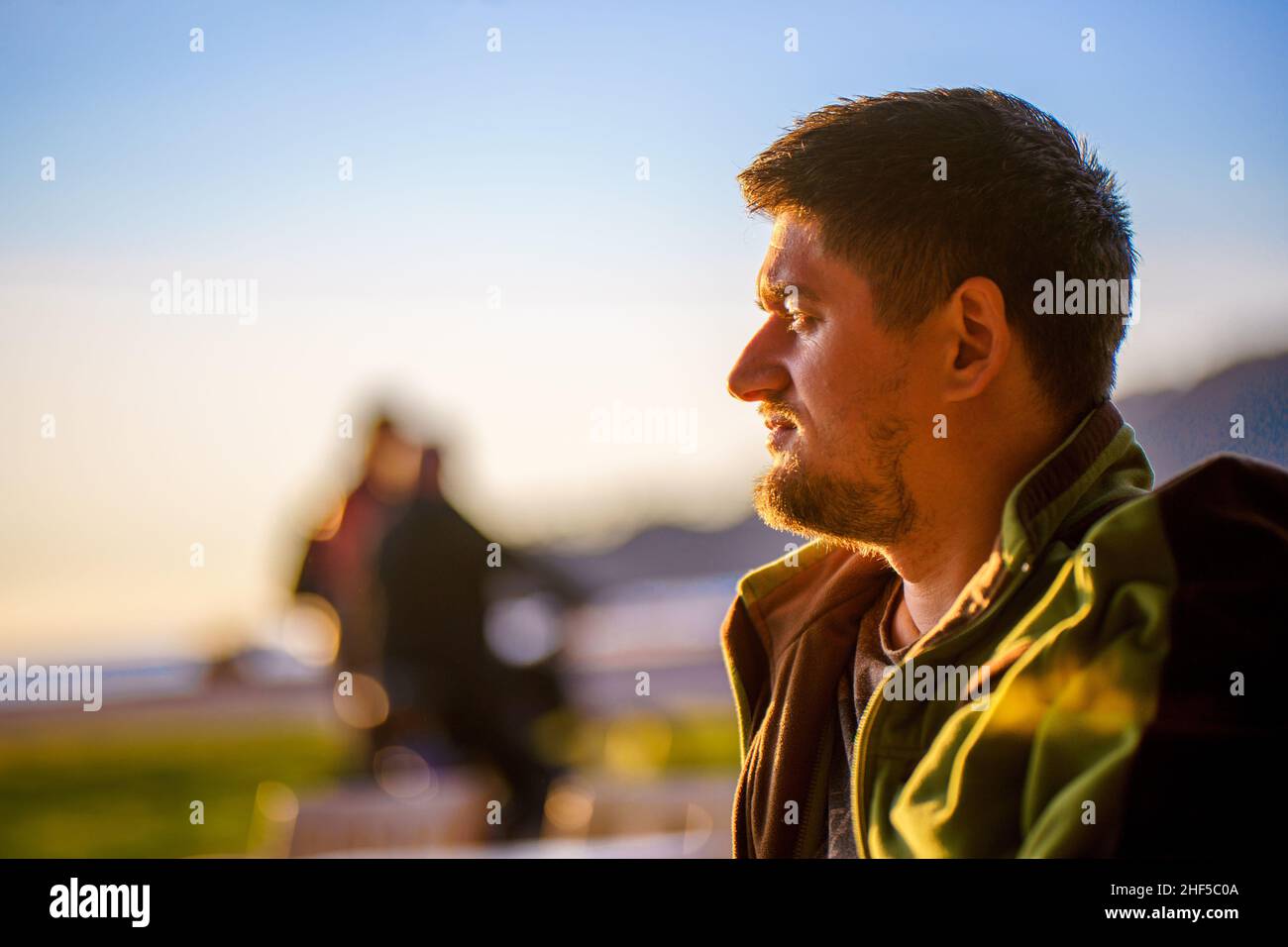 Un turista disfruta de una brillante puesta de sol en la costa del mar de invierno. Hombre joven guapo en primer plano de perfil. Foto de stock