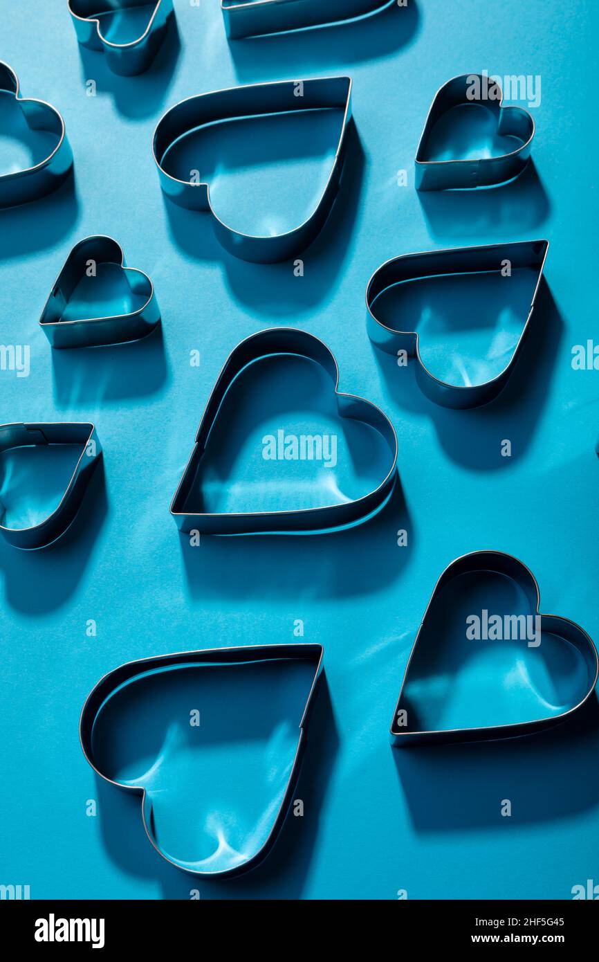 Vista en ángulo de los cortadores de masa en forma de corazón con sombras sobre fondo azul Foto de stock