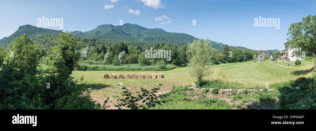 Escena rural con campos verdes, fardos de heno y cielo azul. Parque regional Campo dei Fiori y el pueblo de Brinzio, provincia de Varese, Italia Foto de stock