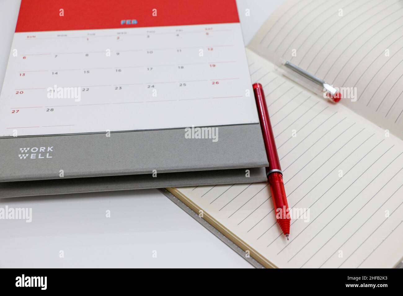 Calendario de febrero de 2022 sobre escritorio blanco con portátil y lápiz rojo Foto de stock