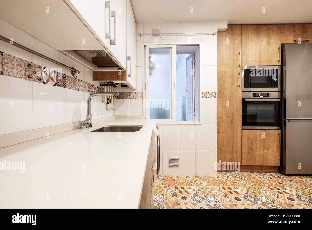 Cocina con muebles de madera combinados con muebles blancos que cubren las paredes desde el suelo hasta el techo y pisos hidráulicos de gres Foto de stock