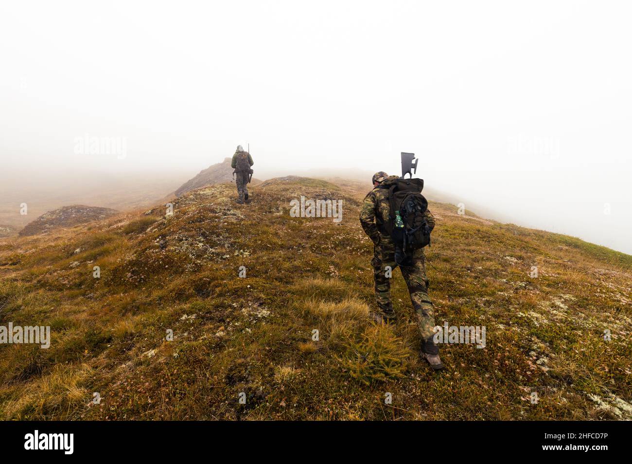 Dos cazadores con ropa de camuflaje caminando por las montañas suizas, en una montaña con niebla Foto de stock