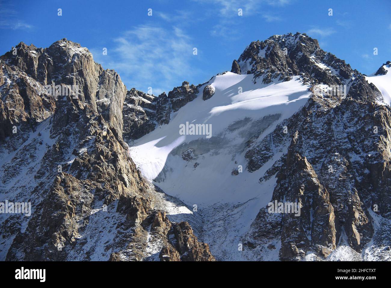 Picos alpinos rocosos coronados de nieve con el glaciar Tuyuk Su en invierno, cuando hace sol Foto de stock